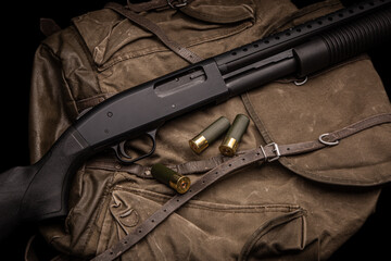 A black 12-gauge pump-action shotgun and ammo are on a canvas backpack. A smooth-bore weapon with a plastic stock. Dark back