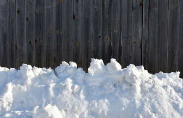 Winter background. A snowdrift on the background of an old fence made of unpainted boards. Lumps of snow. Wood texture