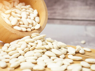 white beans in a wooden cup and spoon are scattered on the table