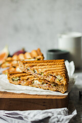 Healthy, natural summer food. Sandwiches with whole grain bread, prosciutto, figs and brie cheese on wooden board napkin on a gray background. Healthy snack. Food to go. Lunch. Brunch ideas