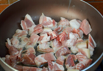 pork meat with layers of fat is stewed in a large frying pan. steam rises from the food being cooked. preparing meat for roasting