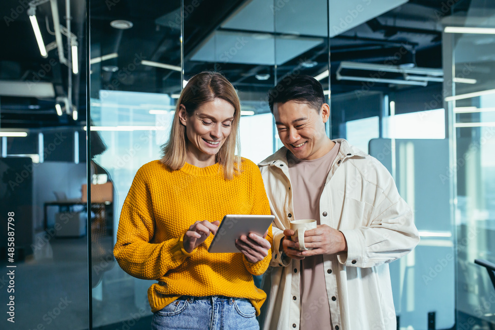 Wall mural two fellow programmers, a man and a woman, happy and smiling looking at the tablet screen, working i