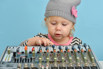 A little girl in a hat adjusts the sound with a mixing console and looks at the controls.
