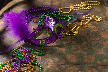 Mardi gras carnivale mask, green, purple, yellow beads on rustic tile background