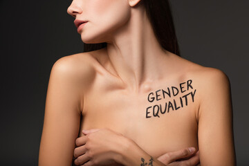partial view of young woman with gender equality inscription on body covering breast with hands isolated on dark grey