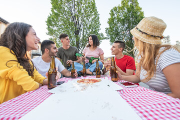 people having fun around a wooden table with take away pizza and bottles of beer, young group of couples singing and playing music to feel carefree and happy, generation z recreation moments