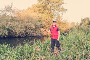 Fisherman in a red vest with a fishing rod on the shore.