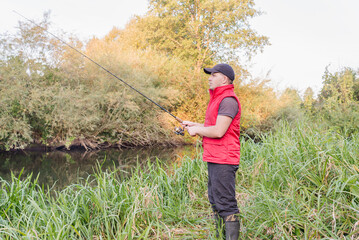 Fisherman in a red vest with a fishing rod on the shore.