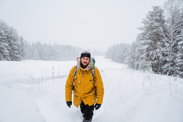 Fototapeta na wymiar Charming traveler walking with hiking backpack in the snowy woods. Bright backpack with equipment. Climbing the mountain in winter. Survival in the wild.