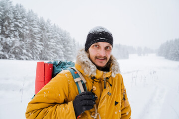 portrait of a merry traveler walking with hiking backpack on the back of the traveler. Snowy forest and rocks. Climbing the mountain in winter. Survival in the wild.