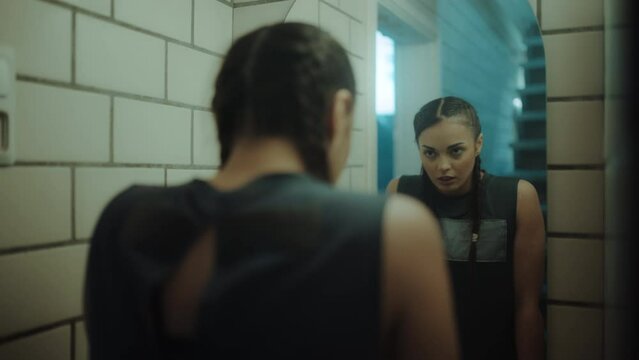 Isolated Badass Female Kickboxer Standing In Front Of The Mirror Looking At Herself, Before Starting Her Training With a Coach at an Old Boxing Gym Studio, Wearing Braids and a Tank Top.
