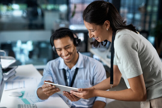 Showing The New Rep The Ropes. Shot Of A Young Man And Woman Using A Digital Tablet While Working In A Call Centre.