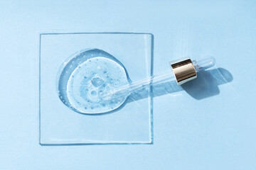 Cosmetic product drops or liquid transparent gel with bubbles on a blue background.