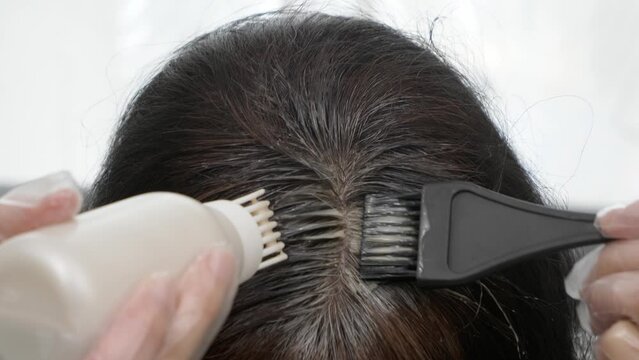 Hair coloring at home. Middle age woman dyeing hair using black brush. Woman colouring her dark hair with regrown gray roots