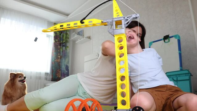 Happy mom and child have fun together, laughing, playing with a toy crane. A mother rolls a toy car on her son's back, the child laughs from tickling. A pleasant family pastime. Slow motion 4k video