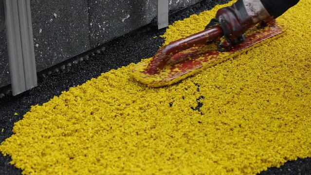 Mason leveling hot rubber coating for playgrounds with trowel, mason hand spreading soft rubber crumbs. Outdoor soft coating and floor covering for sports. Rubber mulch for safety. selective focus.