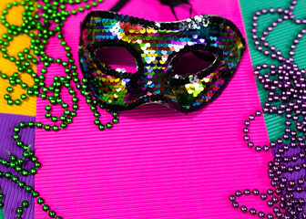 Mardi gras mask and beads in pile on purple background.