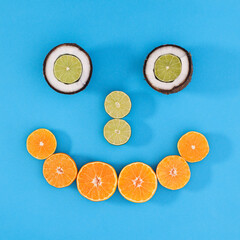 Creative smiley face made of citrus fruits and coconut on cyan or blue background. Minimal flat lay