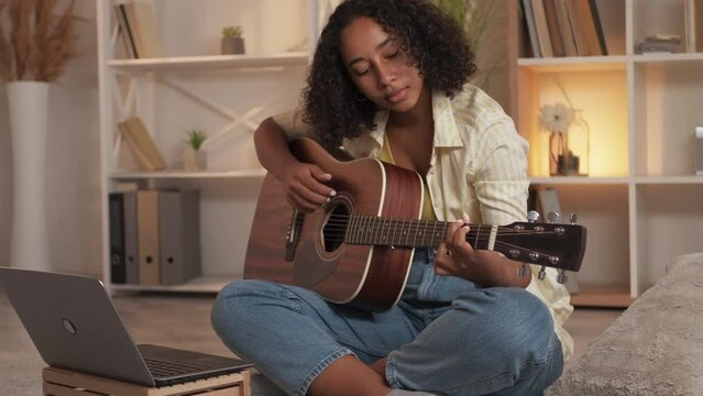 Guitar course. Internet music class. Creative hobby. Inspired young woman guitarist learning string instrument chords lesson online at laptop at home.