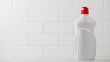 A mockup of a white plastic bottle with liquid dishwashing detergent with a white tiled background. Copy space.
