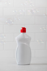 A mockup of a white plastic bottle with liquid dishwashing detergent with a white tiled background with bubbles 