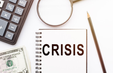 CRISIS text on notepad with with calculator, pencil and magnifier on the white background