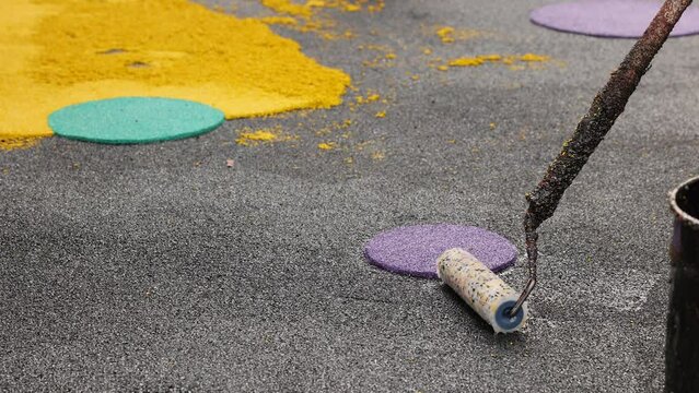 Rubber coating for playgrounds applied on the surface by a steel roller tools worker. PDM rubber granules. Floor covering for sports. Rubber mulch for safety and injury prevention. Selective focus.