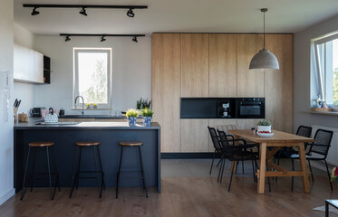 Luxurious interior of kitchen with wooden furniture, dining table and chairs and counter with stools.