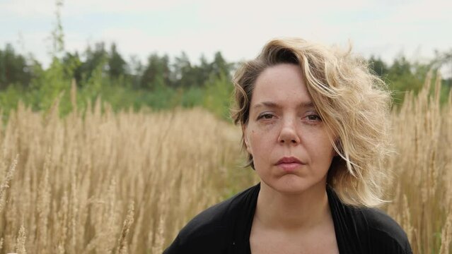Portrait of a forty-year-old blonde woman. A woman in black clothes in a dry field. Slow motion portrait
