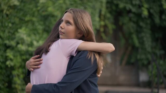 Hypocritical insincere teenage girl hugging friend with annoyed facial expression. Portrait of unhappy Caucasian teenager meeting annoying friend outdoors in park on summer spring day. Slow motion