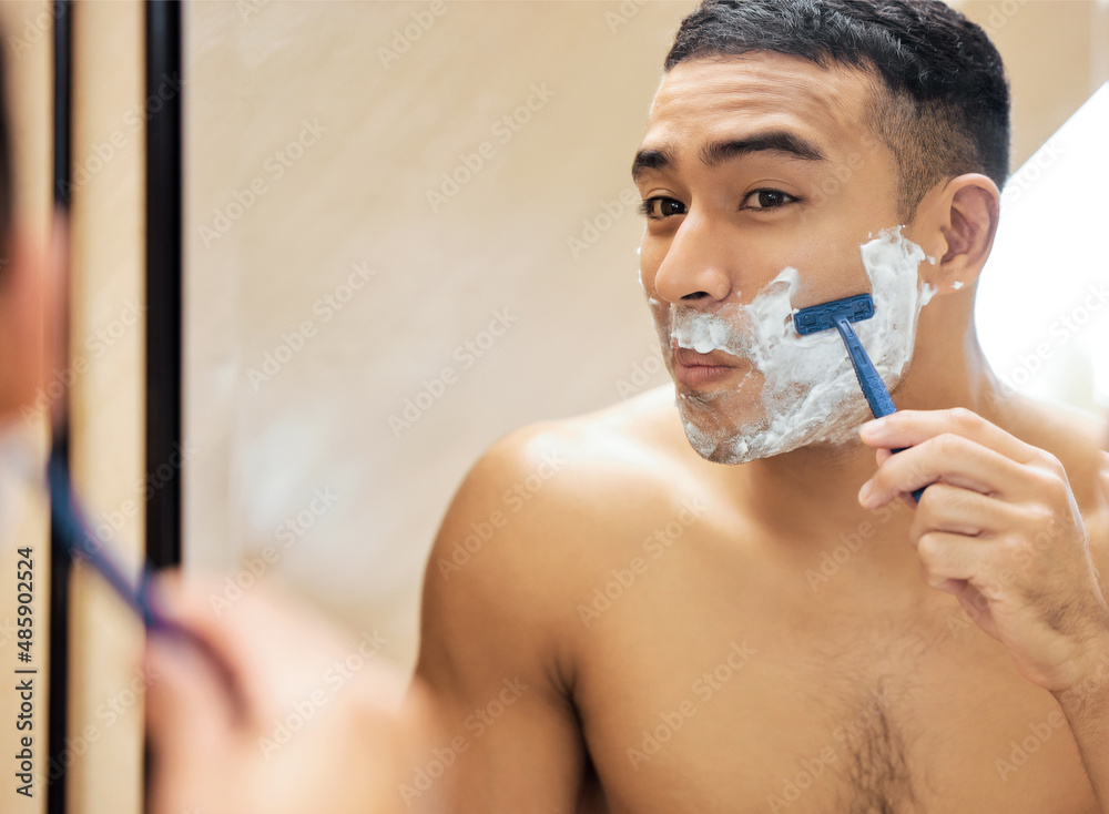 Poster lets put this razor to the test. shot of a young man looking in the mirror while shaving his beard.
