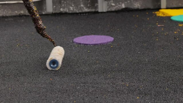 Rubber coating for playgrounds applied on the surface by a steel roller tools worker. PDM rubber granules. Floor covering for sports. Rubber mulch for safety and injury prevention. Selective focus.