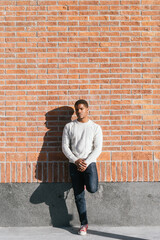 Fototapeta na wymiar Black student man using red phone on a street. Modern male with white sweater leaning against a wall.