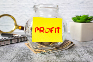 A glass jar with coins and the inscription PROFIT on a wooden table. Budget for investing.
