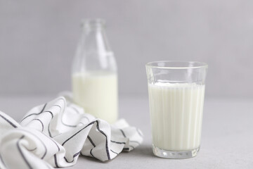 A glass of fresh milk, a bottle and textiles on a gray background. Selective focus.