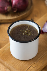 Homemade healthy bone broth with spices in a white mug on a wooden board.
