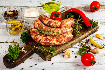 Bratwurst or sausages with spices and greens on a cutting board. On a white wooden table.
