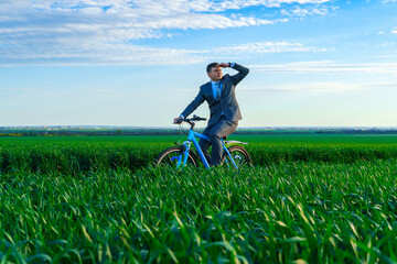 business concept - A businessman rides a bicycle on a green grass field, looks into the distance, dressed in a business suit, he has a briefcase and documents