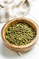 Dried green peppercorn. Dry green pepper spice in bowl on white table.