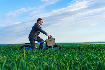 business concept - A businessman rides a bicycle on a green grass field and in a hurry, dressed in a business suit, he has a briefcase and documents