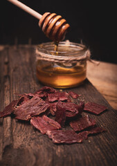 Beef jerky on wooden cutting board, vertical view. Dried beef meat chips and honey, composition on...