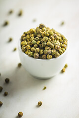 Dried green peppercorn. Dry green pepper spice in bowl on white table.