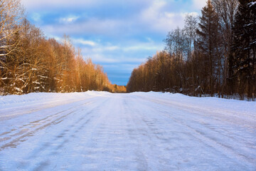 Obraz premium Winter asphalt road covered with snow and sprinkled with sand in bright sunlight.