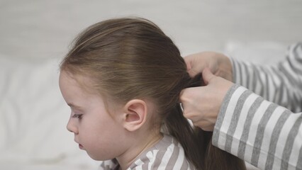 Mother braids daughter brunette long hair into hairstyle