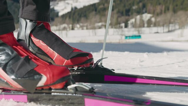Cross country skier legs standing on skis, putting the toe of the ski boot in the notch on the ski, and hooking the metal bar on the boot, close up shot.