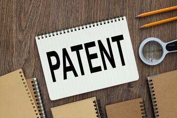 Patent. Open notebook near a magnifying glass and pencils on wooden desk