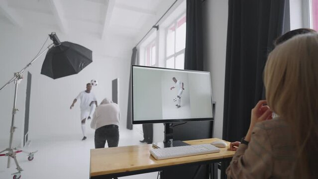 Behind-the-scenes photo shoot: A photographer in a photo studio uses a flash for photos of a black professional football player. Photo shoot in the studio of a sports magazine, advertising