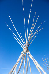 Authentic Native American teepee frame poles rising against a sharp blue winter sky © JD