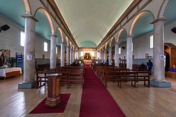 Innenansicht einer alten Holzkirche auf Chiloe samt eines weißen Säulenganges, Rundbögen und...