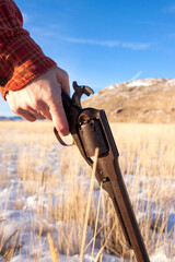 Woman's hand holding a Civil War revolver in the Wild West of a Wyoming winter, her red sleeve...